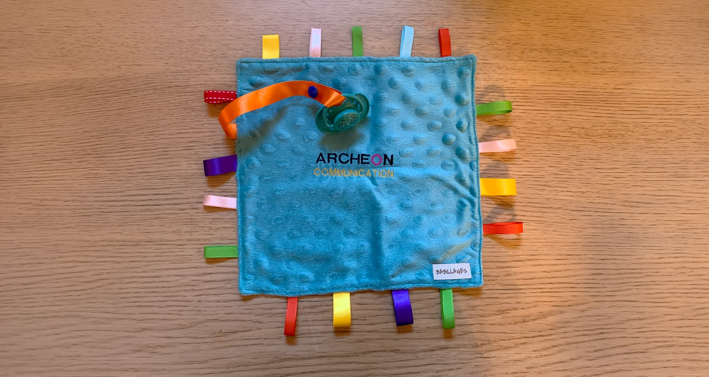 Photographie en gros plan d'articles personnalisés de la marque La Sardine Lotoise : un mug blanc avec prénom brodé ou personnalisé, un petit doudou en tissu de qualité avec détails soignés, et une serviette ou transats nominatif, tous disposés ensemble de manière artistique et professionnelle sur une surface neutre. L'image doit montrer la qualité artisanale, l'authenticité made in France et le soin apporté aux finitions, reflétant le contrôle qualité rigoureux de l'entreprise. Éclairage naturel et professionnel mettant en valeur les détails de personnalisation.